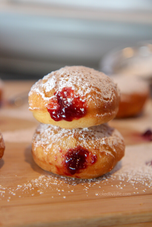 jelly donuts with powdered sugar stacked on top of a wooden board