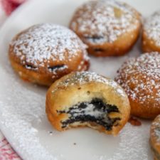 deep fried Oreos with powdered sugar on a white plate with one half eaten cookie and a red and white towel on the side.