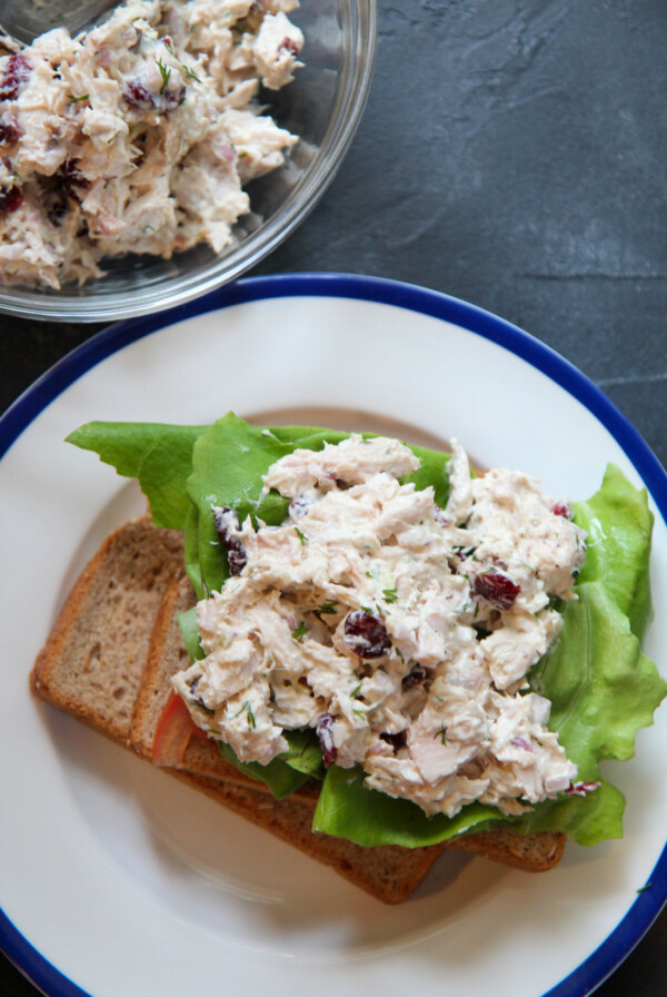 chicken salad sandwich with lettuce on a plate with a bowl of chicken salad in the background