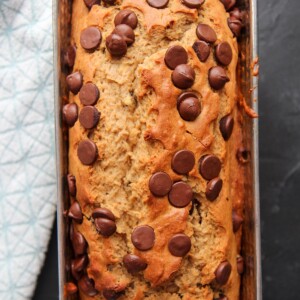chocolate chip banana bread in a load pan on a black surface with a blue towel on the side.