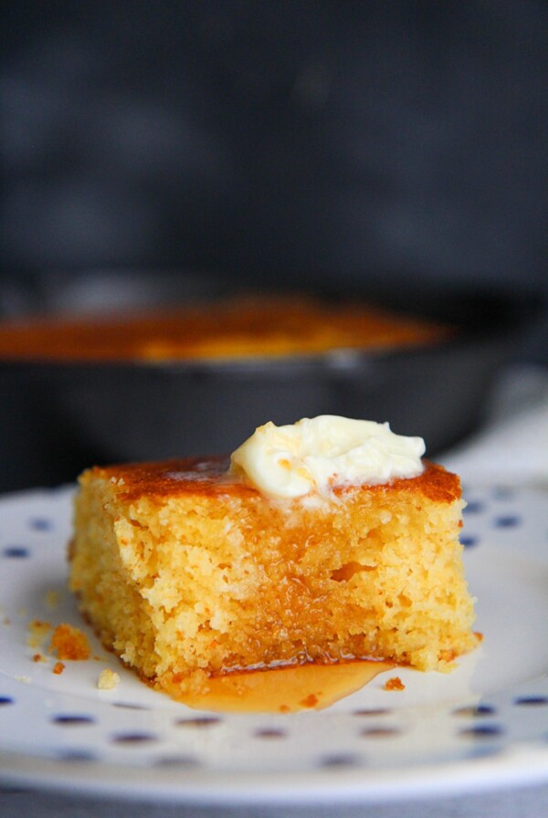a slice of cornbread with butter and honey on a plate.