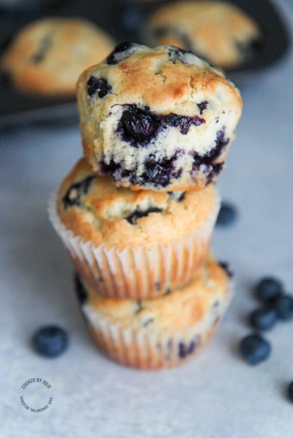 three blueberry muffins stacked with fresh blueberries on the side