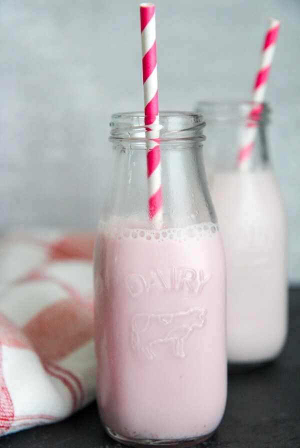 two milk jugs filled with strawberry milk and pink and white straws.