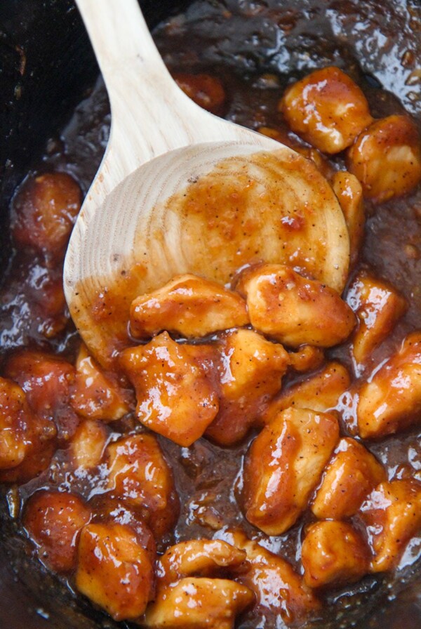 orange chicken in the slow cooker with a wooden spoon.