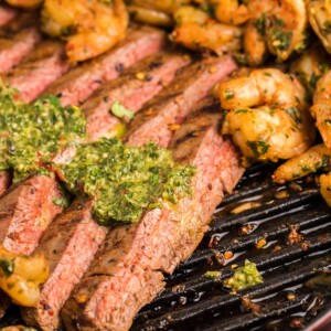 slices of steak with chimichurri on top and shrimp on the side.