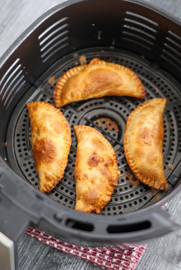 four cooked ground beef empanadas in the air fryer basket.