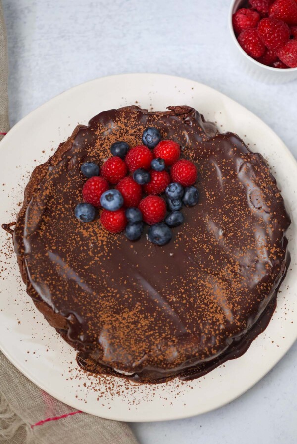 whole flourless chocolate cake with blueberries and raspberries on top.