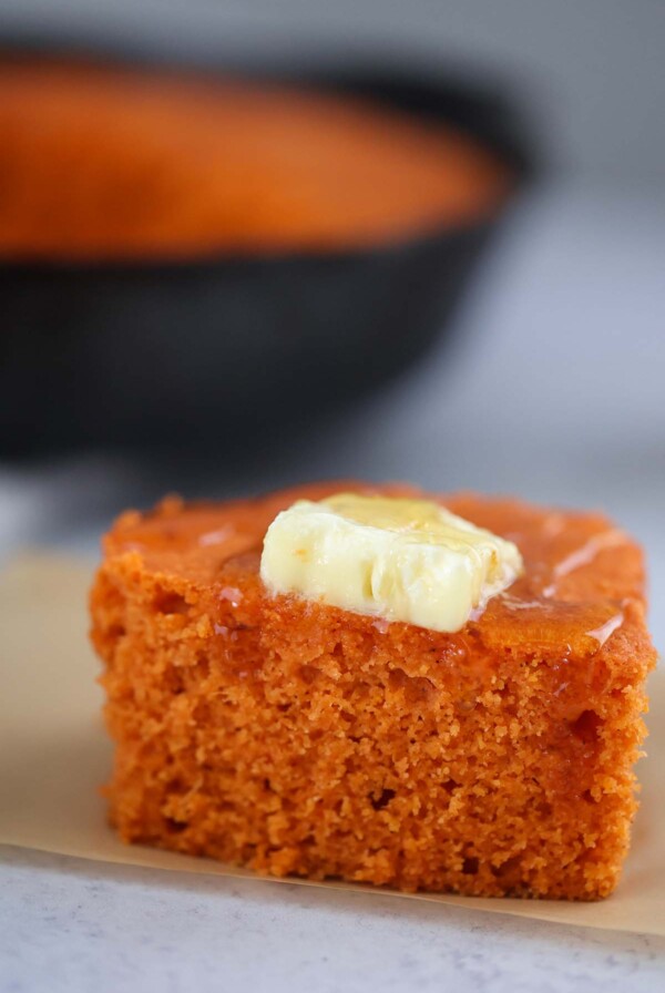 a square slice of sweet potato cornbread with butter and honey on top.