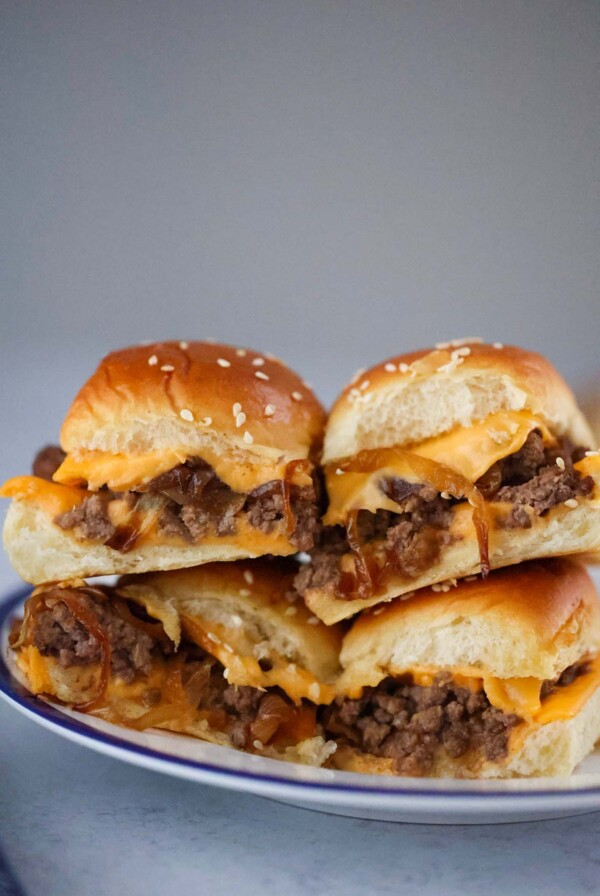 four cheeseburger sliders with caramelized onions on a plate.