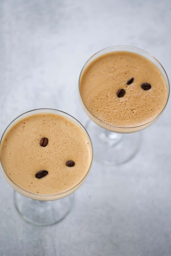 Two espresso martinis with foamy tops and coffee beans.