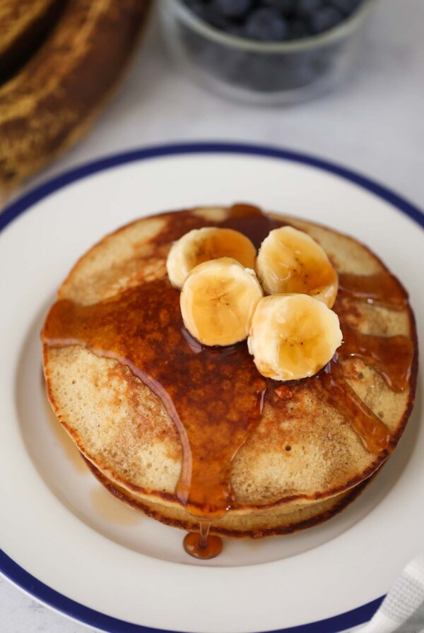 A stack of banana oatmeal pancakes with sliced bananas and maple syrup on top.