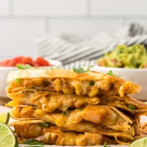 four shrimp quesadillas stacked with limes and guacamole on the side.