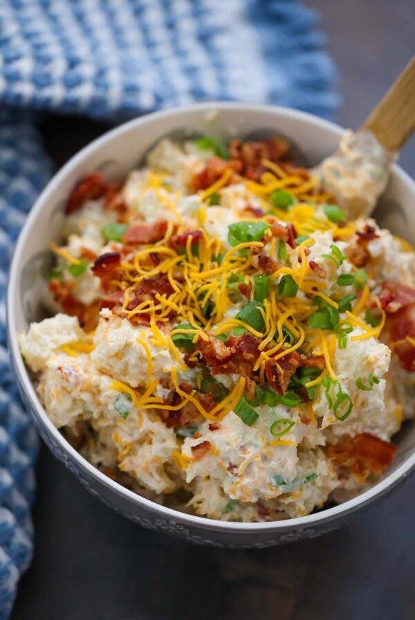 loaded baked potato salad in a bowl with a wooden spoon.