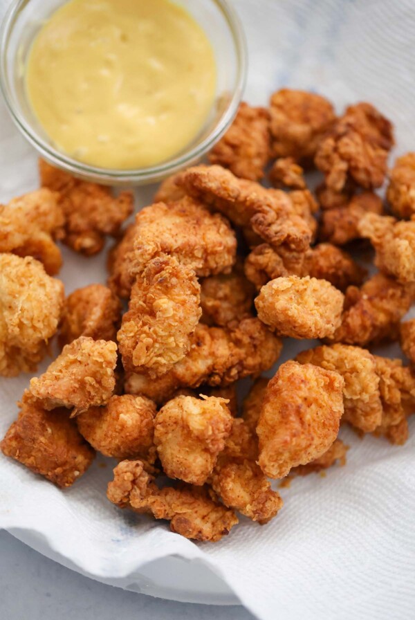 popcorn chicken on a plate with honey mustard on the side.