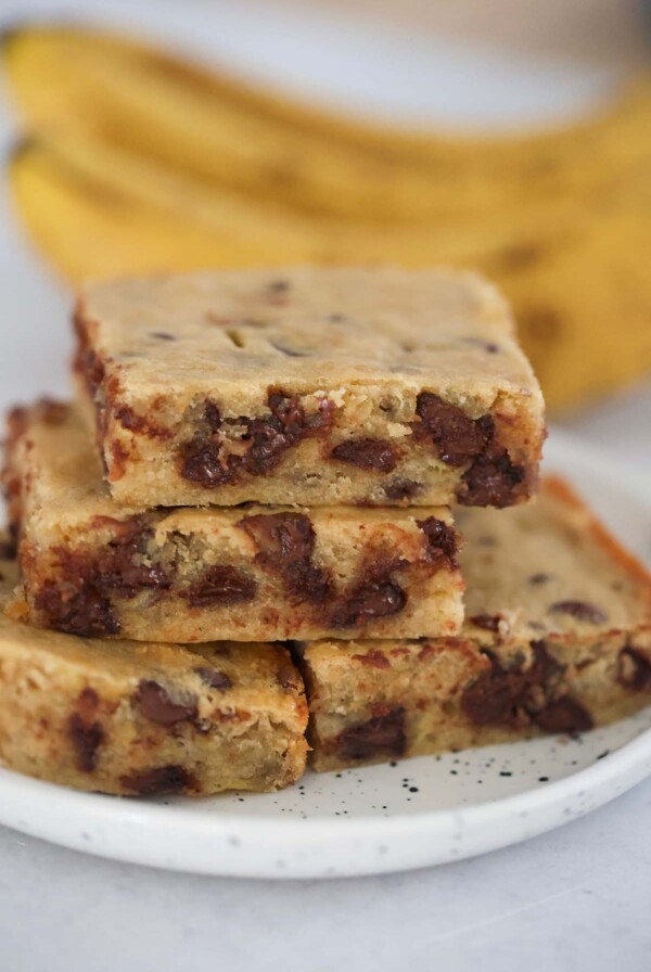 chocolate banana bars on a plate with ripe bananas in the background.