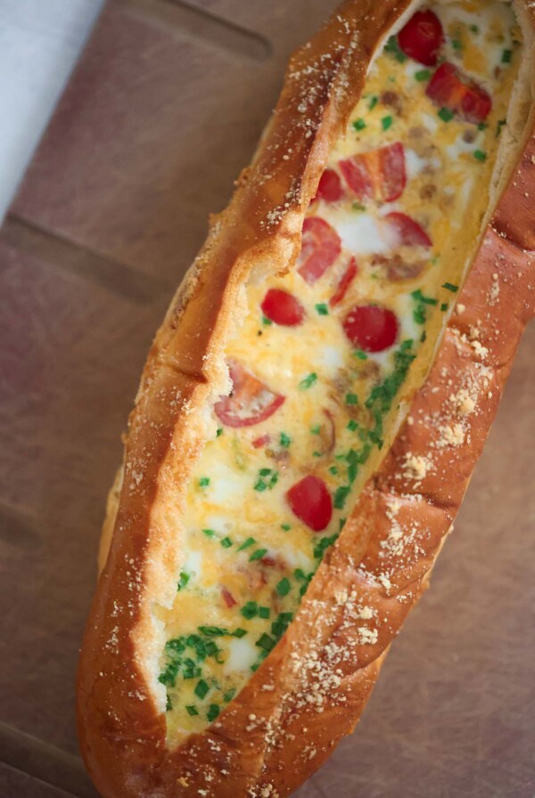 baked eggs with tomatoes, chives, and cheese inside of a loaf of bread.