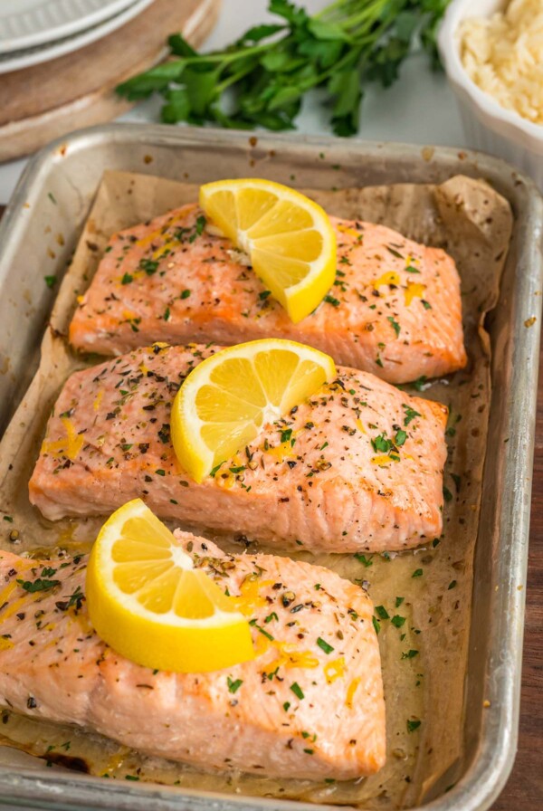 three salmon fillets with lemon wedges on top.