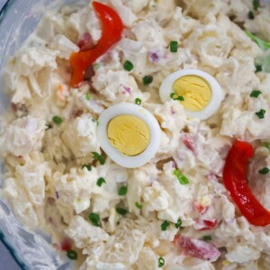 Potato salad with boiled egg slices and pimientos on top.