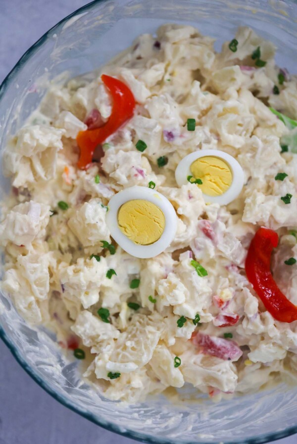 Potato salad with boiled egg slices and pimientos on top.