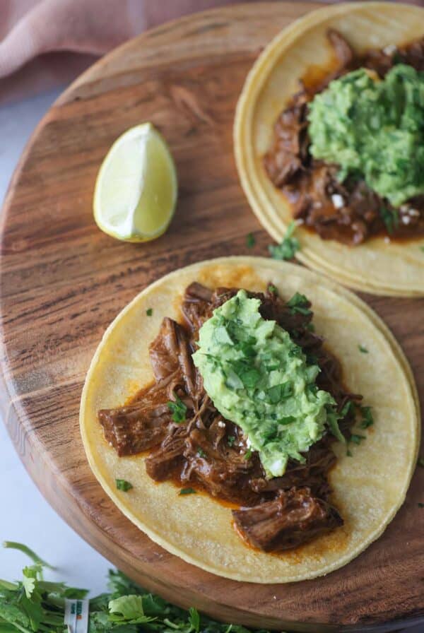 two shredded beef tacos on a wooden board with a lime wedge on the side.