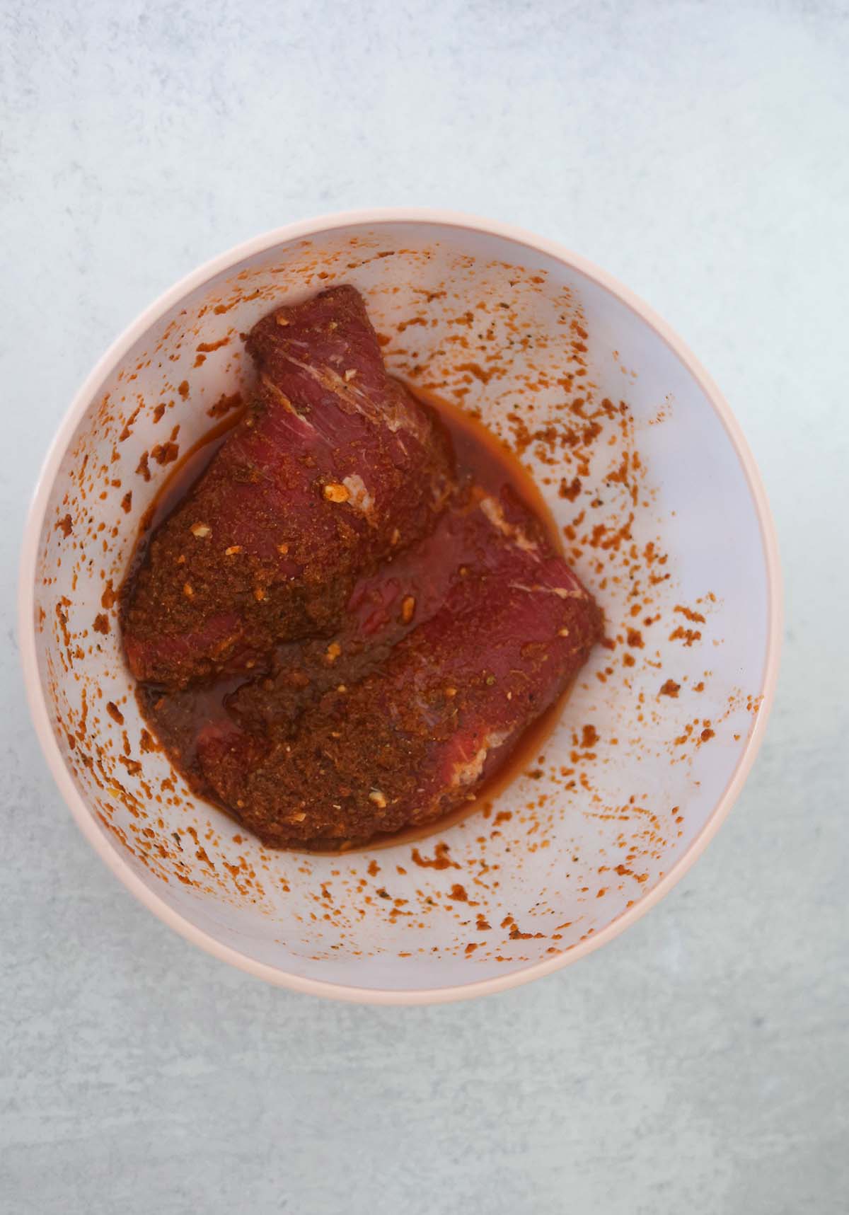 Raw flank steak marinating in a white bowl. 