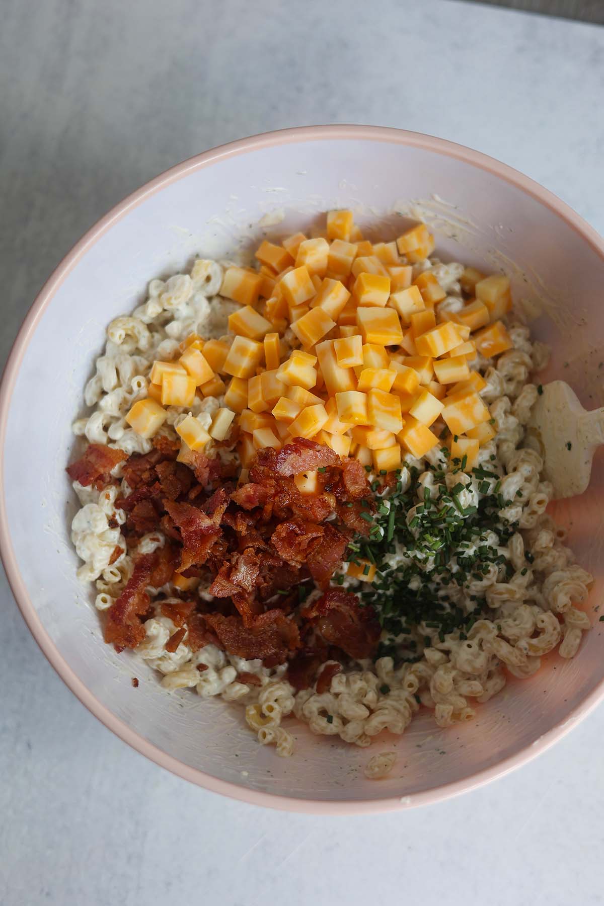 Macaroni, cheese, bacon, and chives in a bowl with a spatula. 