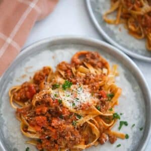 two plates of fettuccine bolognese with a towel on the side.