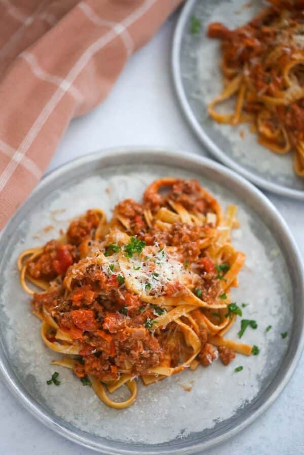 two plates of fettuccine bolognese with a towel on the side.