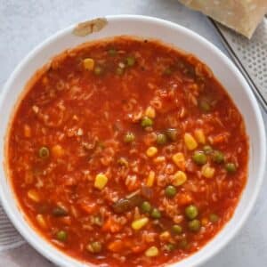 Alphabet soup in a white bowl with a block of parmesan cheese on the side.