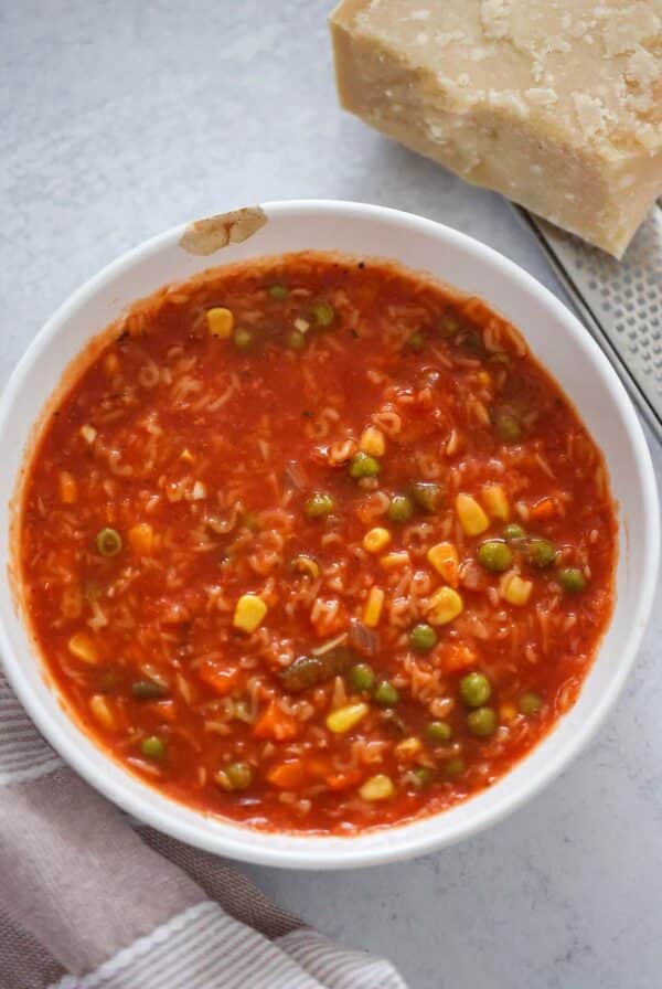 Alphabet soup in a white bowl with a block of parmesan cheese on the side.