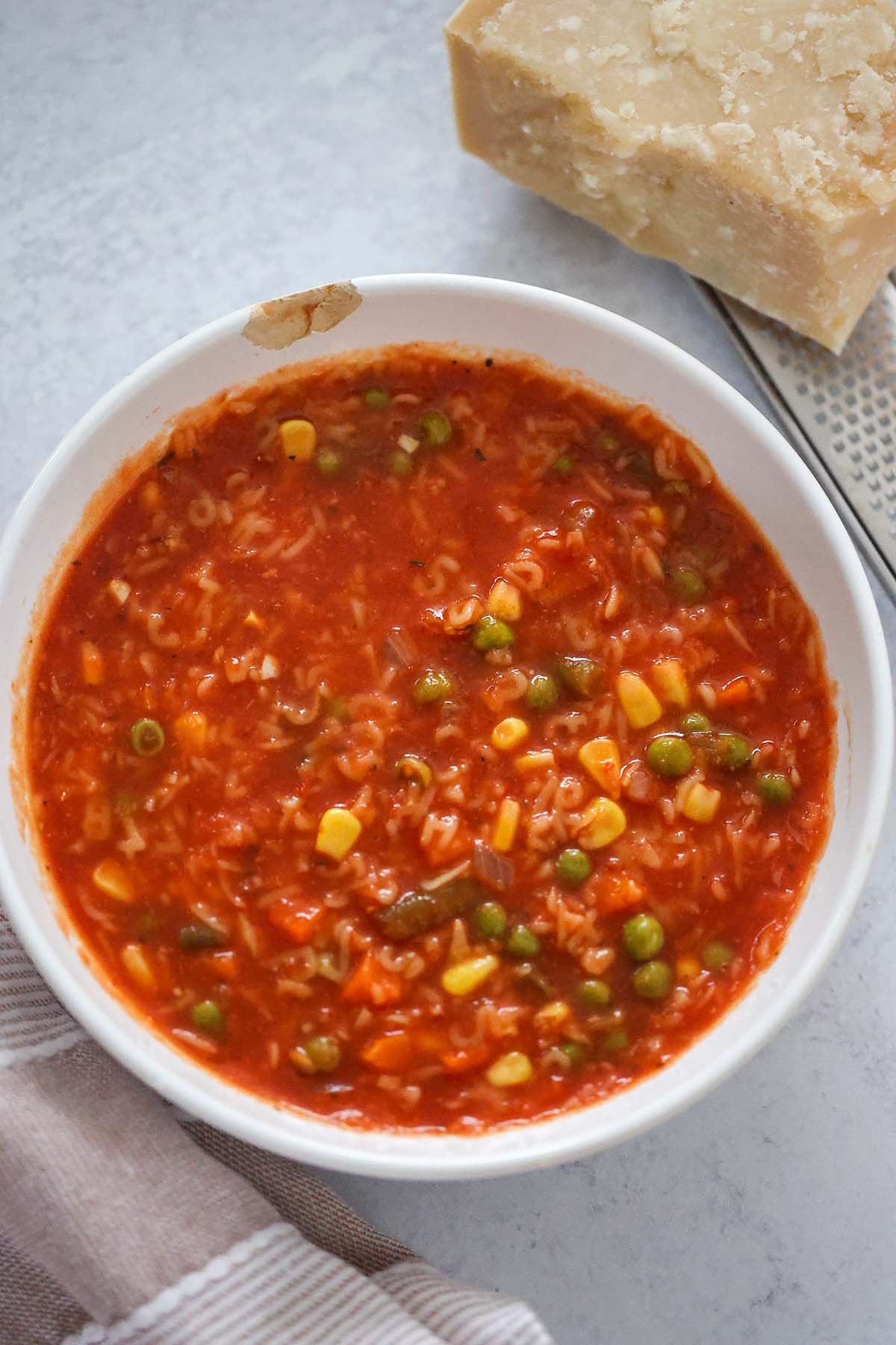 Alphabet soup in a white bowl with a block of parmesan cheese on the side. 